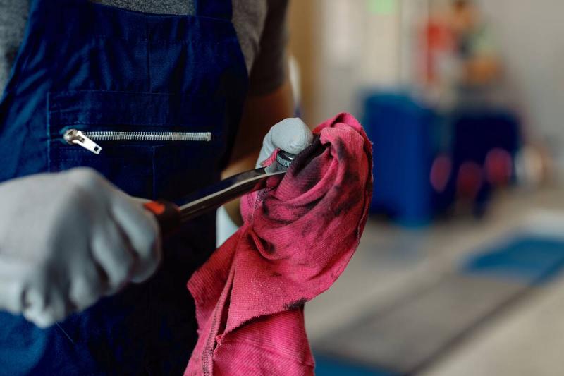 Close up of mechanic wiping off oily tool on rag. 