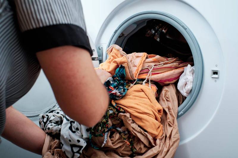 Hands putting clothes in washing machine. 