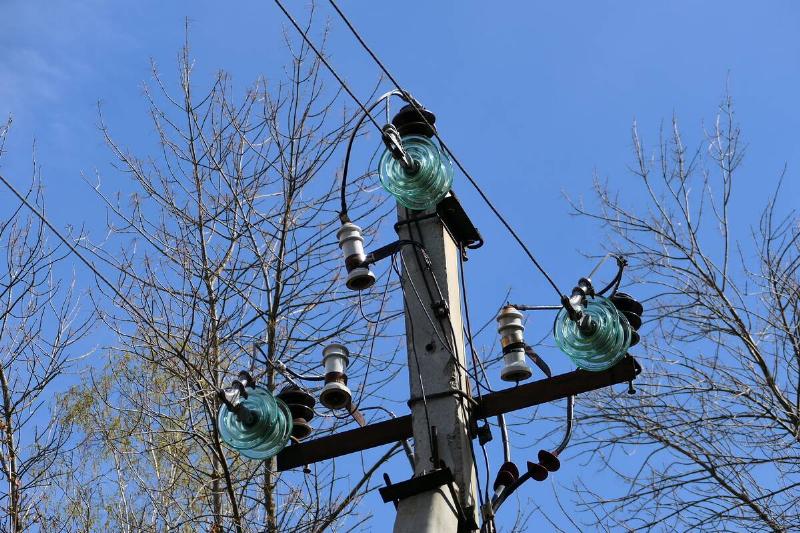 Close-up of high-voltage power lines and power pylons against a blue sky.