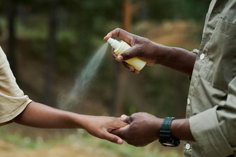 Man spraying DEET on other person's arm.