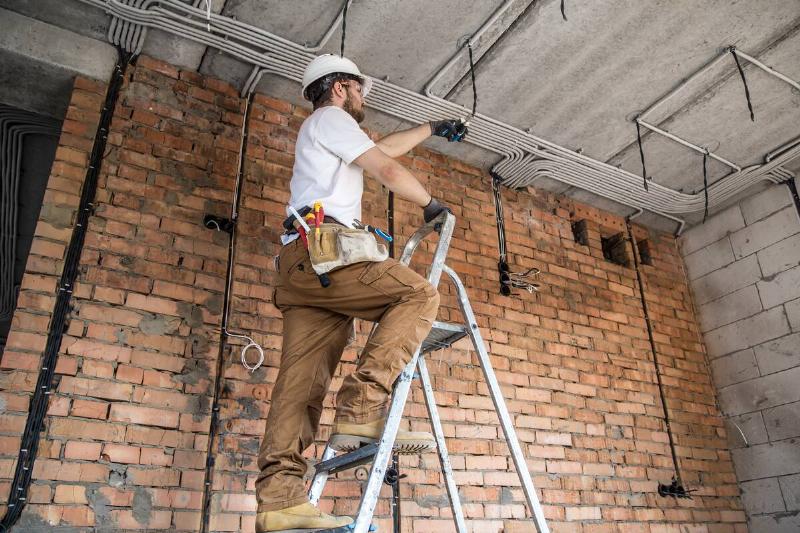 Electrician with tools, with three points of contact on ladder. 