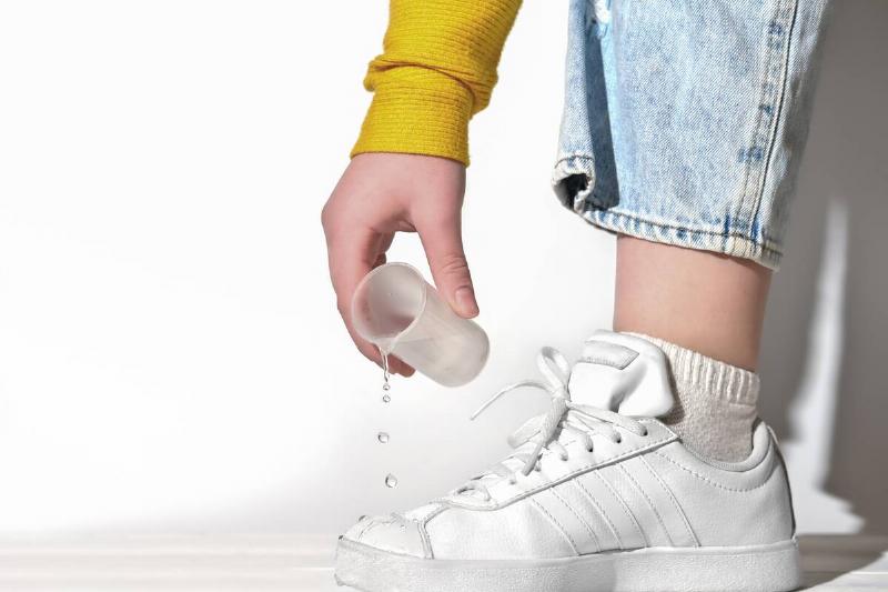 Hand pouring tobacco water on white shoes.