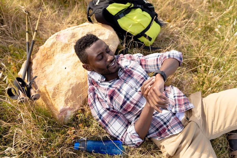 Hiker checks watch while laying down on rock. 