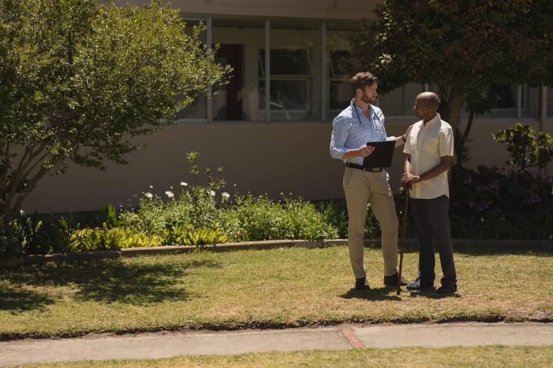 Man with clipboard talking to another man while standing on front lawn.
