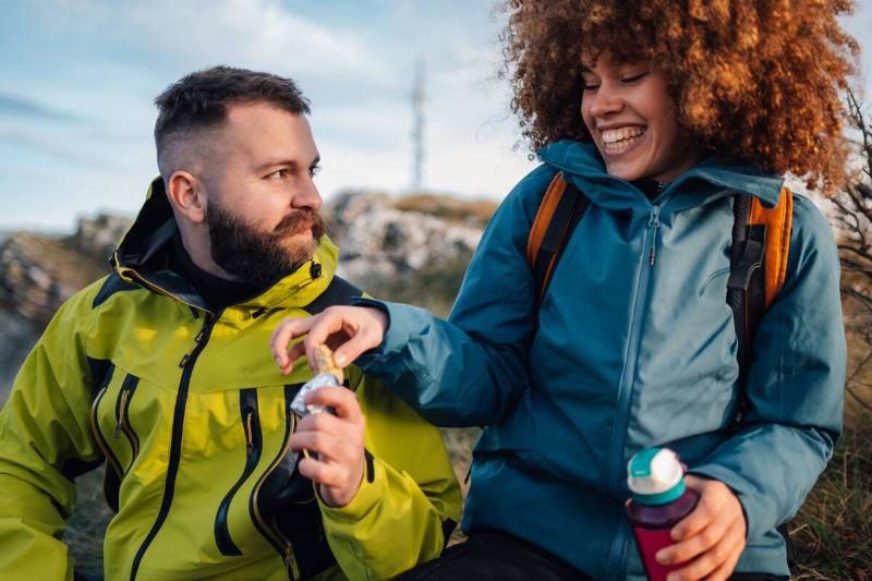 Man and woman sharing protein bar on a hike. 