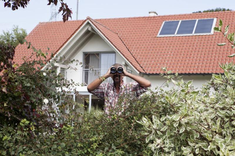 Man looking through binoculars over hedge.