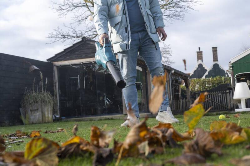 Man using an electric blower to tidy up leaves in the garden of his home.