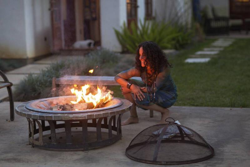 Woman crouching in front of patio fire at dusk.