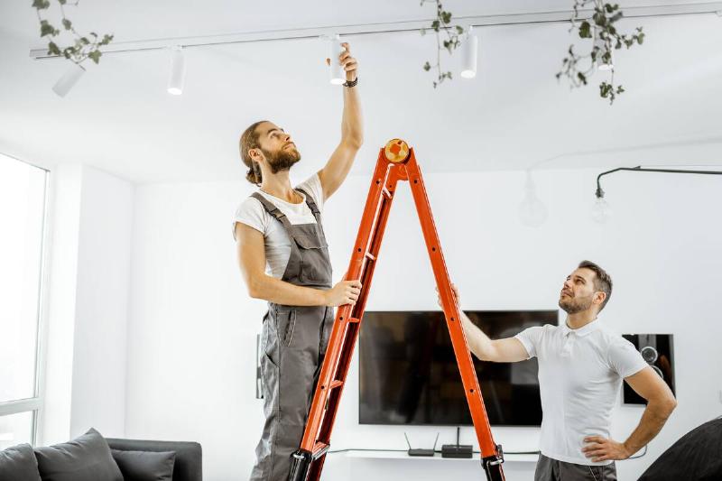 Two men installing lights on a ladder. 
