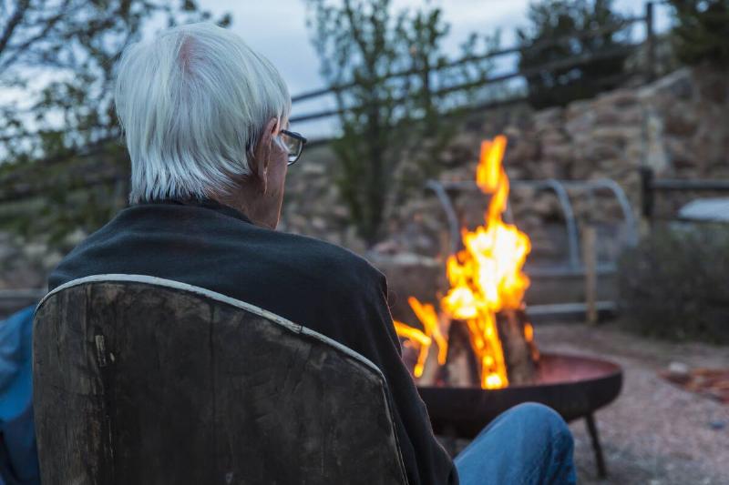 Rear view of man watching fire in backyard fire pit.