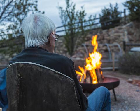 Rear view of man watching fire in backyard fire pit.