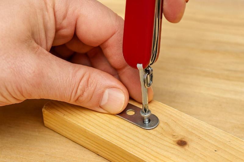 Hands using a Swiss Army knife to screw in a screw. 