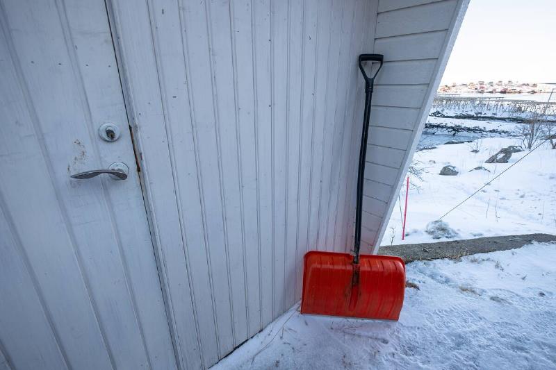 Red shovel outside of a wooden garage.