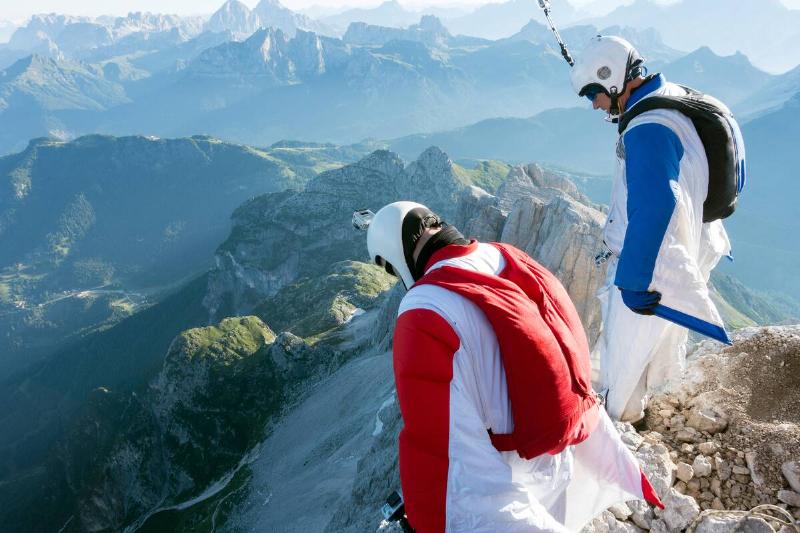 Two male BASE jumpers standing on edge of mountain looking down, Dolomites, Italy.