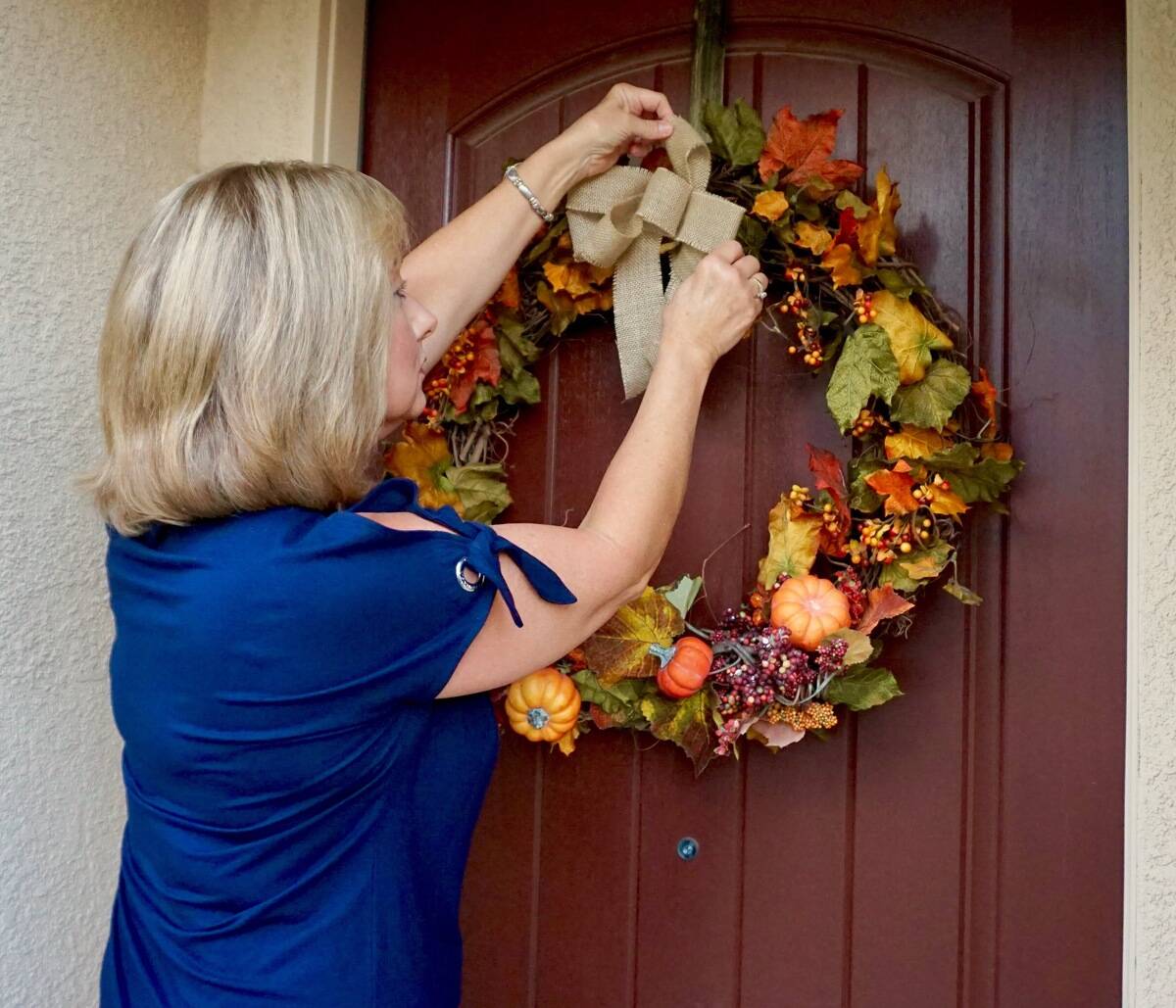 Woman hanging fall wreath on front door. 