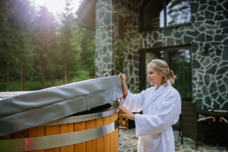 A woman in bathrobe opening cover of hot tub.