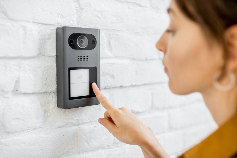 Woman rings the house intercom with a camera installed on the white brick wall.