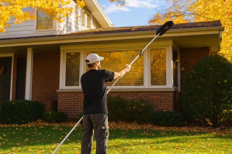 Man using a rake to clean gutters from the ground.