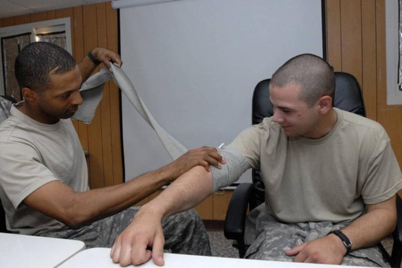 Soldier using compression gauze on soldier's arm.