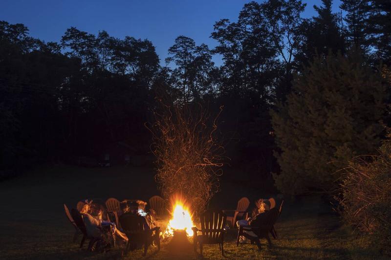 A group of people seated around a campfire at dusk.