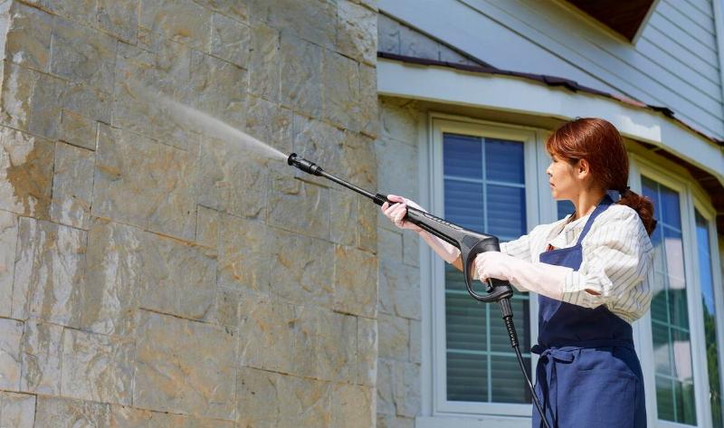A woman using a pressure washer to clean a stone wall.