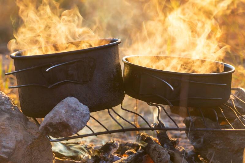 Touristic kettle on fire of burning campfire in camping in the hike. Cooking food in forest on wooden firewood.