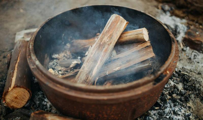 A metal firepit, smoking, with some logs in it.