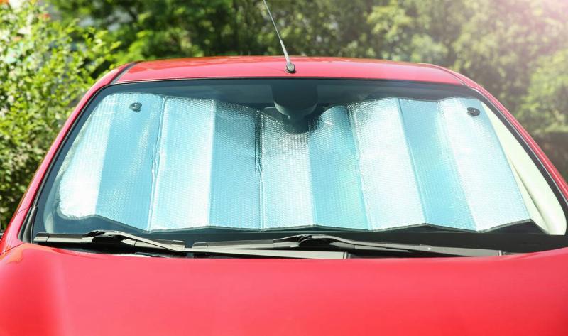 A red car with a reflective cover in the windshield.