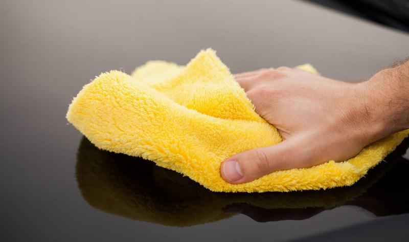A hand wiping a surface with a yellow microfiber cloth.