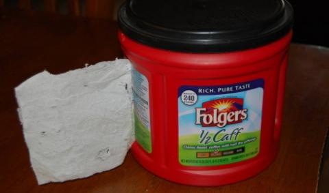 A folgers tin with a square of toiler paper coming out of the side.