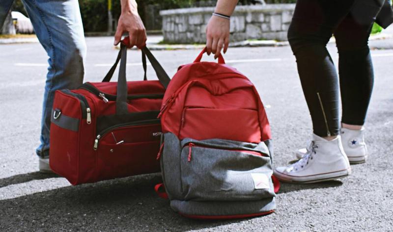 Two people picking up their bags off the ground, one duffle bag and one backpack.