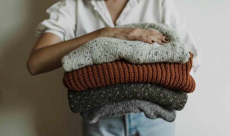 A woman holding a stack of chunky knit sweaters.