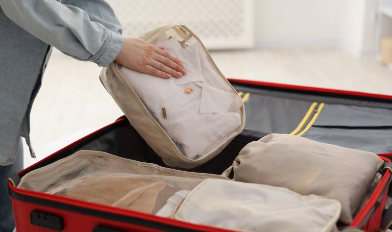 A woman putting a packing cube into a suitcase.