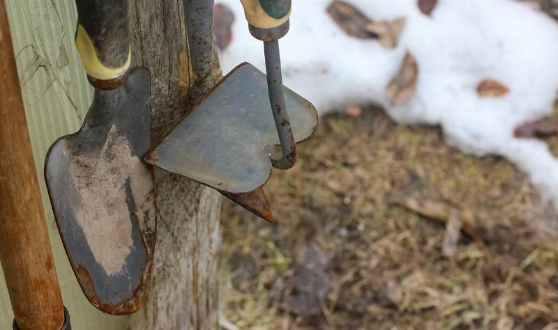 Some rusty garden tools hanging on a post.