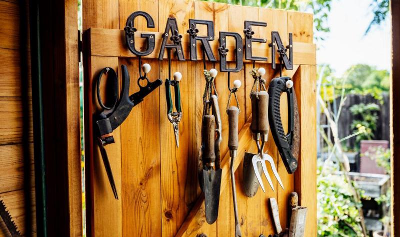 Garden tools hanging on the door of a shed, a metal sign that reads 'GARDEN' above them.