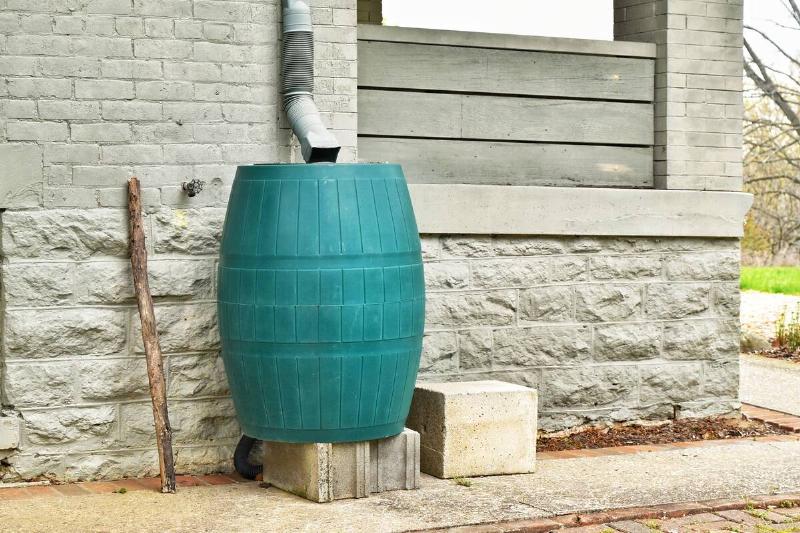 A green plastic rain barrel next to a grey home wall.