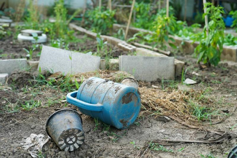 A dirty watering can and plastic plant holder on the ground.