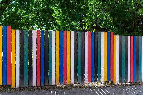 Colorful wooden fence along a sidewalk in a vibrant urban neighborhood on a sunny day
