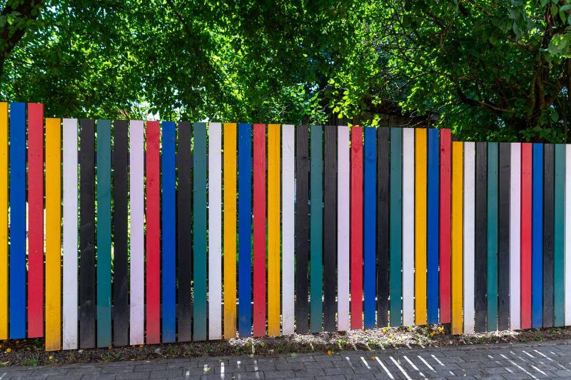 Colorful wooden fence along a sidewalk in a vibrant urban neighborhood on a sunny day