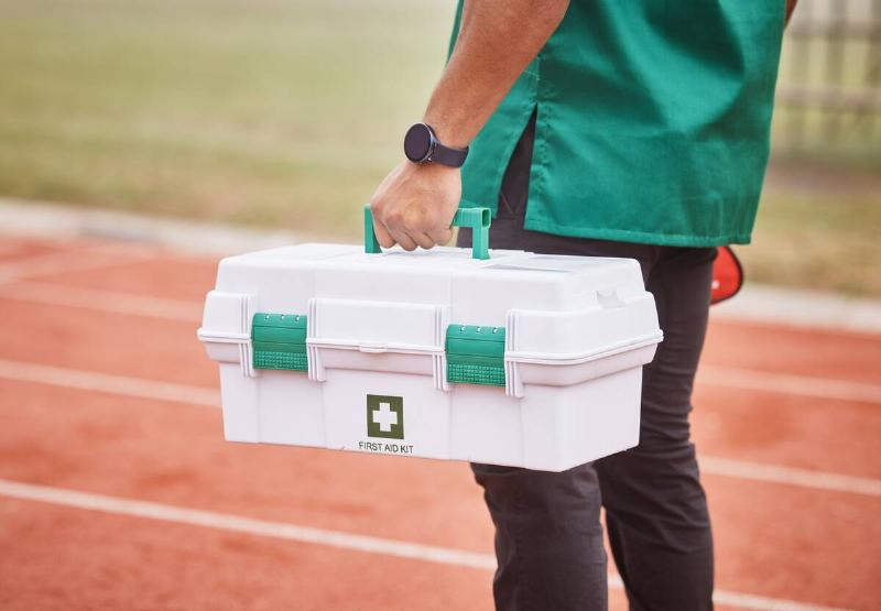 A person standing on a running track with a large, hard-case first aid kit in hand.