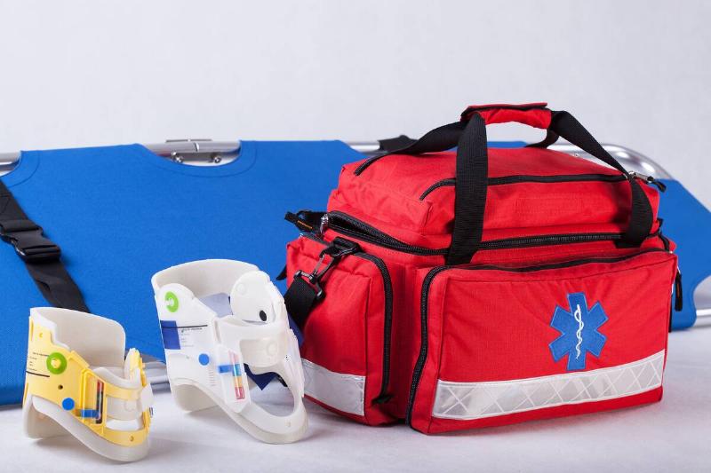 A duffle bag first aid kit made with emergency responders in mind, a gurney behind it and two neck braces beside it.