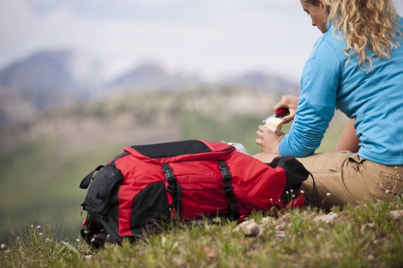 Young woman sitting on grass with red first aid backpack.