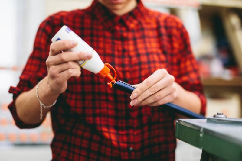 Woman worker putting glue to stick wooden frame.