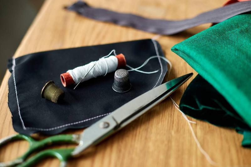 Sewing supplies on a wooden table: sewing thread, scissors, pieces of cloth, needles, centimeter, pattern.