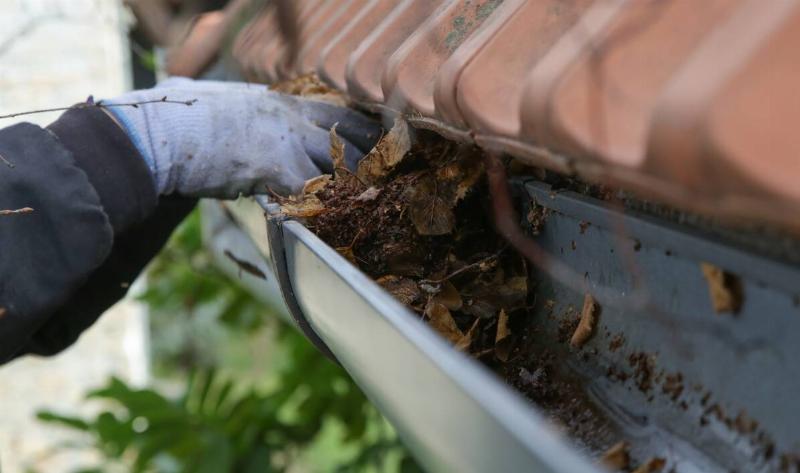 A gloved hand clearing debris out of a gutter.