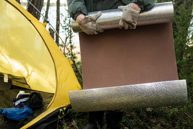 Man rolling up reflective mat to go inside of tent.