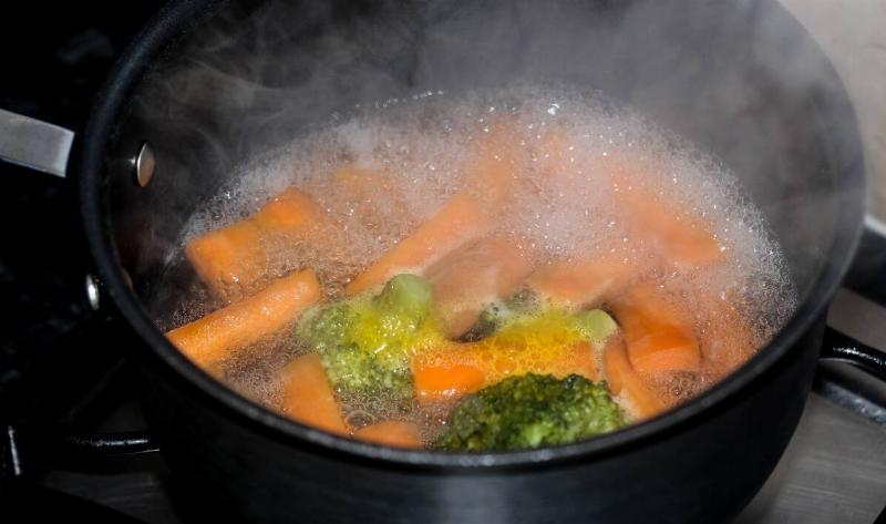 A pot of boiling water with carrots in broccoli.