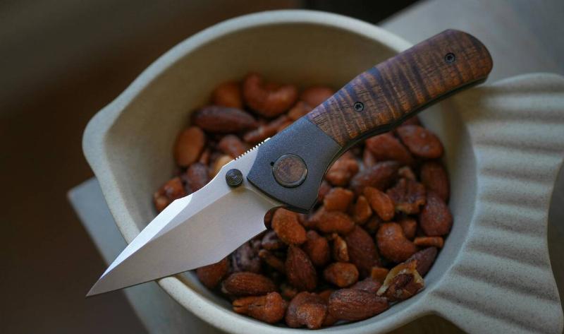 An unfolded pocket knife atop a bowl of almonds.
