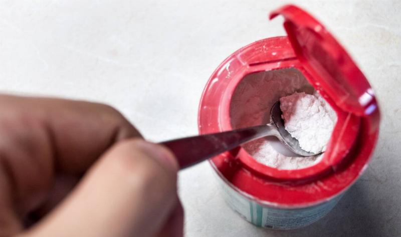 A hand using a spoon to spoon out some baking soda.