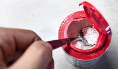 A hand using a spoon to spoon out some baking soda.